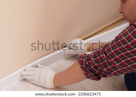 Man installing plinth on laminated floor in room, closeup Royalty-Free Stock Photo #2330623471