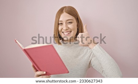 Young blonde woman smiling confident reading book doing thumb up gesture over isolated pink background