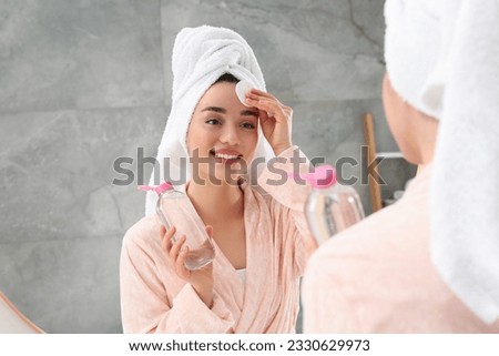 Beautiful woman in terry towel removing makeup with cotton pad near mirror indoors Royalty-Free Stock Photo #2330629973