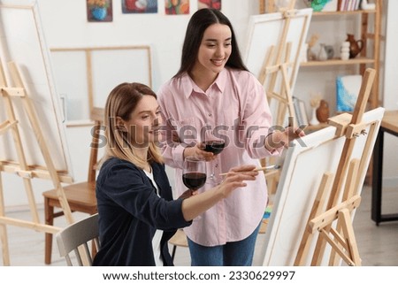 Artist and her student with glasses of wine having painting class in studio. Creative hobby