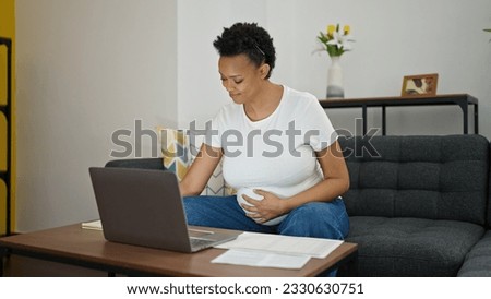 Young pregnant woman sitting on sofa doing online work at home