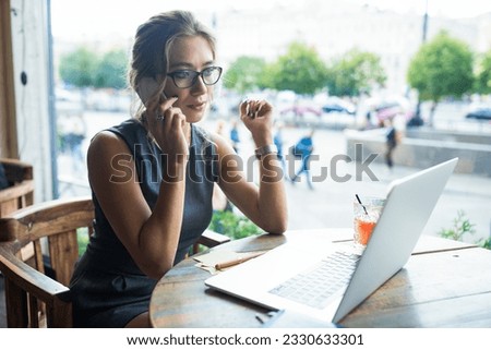 Confident woman successful resume writer having cell telephone conversation while sitting in coffee shop during free time. Female student having online education via notebook gadget 