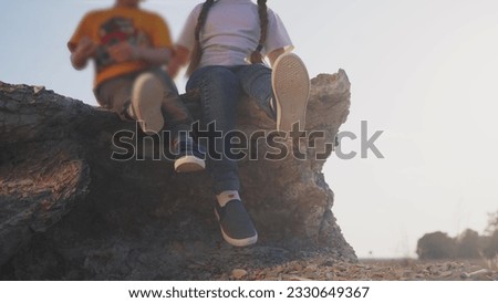 baby children sit on the rocks in the park. happy family kid dream concept. legs close-up baby children dangle their legs rest sit on the rocks at sunset. children tourists in lifestyle mountains Royalty-Free Stock Photo #2330649367