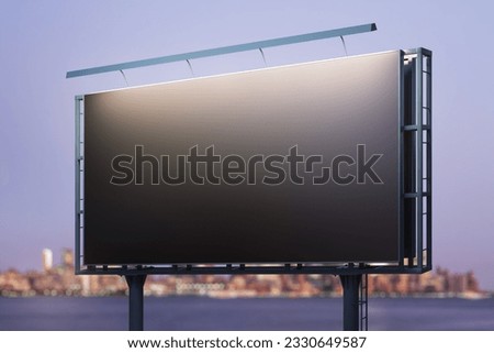 Blank black billboard on city buildings background at night, perspective view. Mockup, advertising concept
