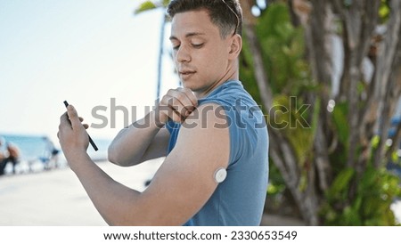 Young hispanic man tourist measuring glucose using smartphone and freestyle at street