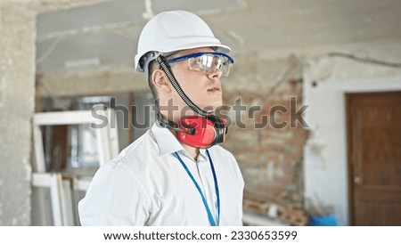 Young hispanic man architect wearing headphones standing with relaxed expression at construction site