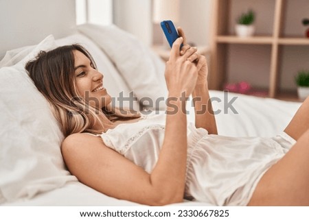 Young woman using smartphone lying on bed at bedroom