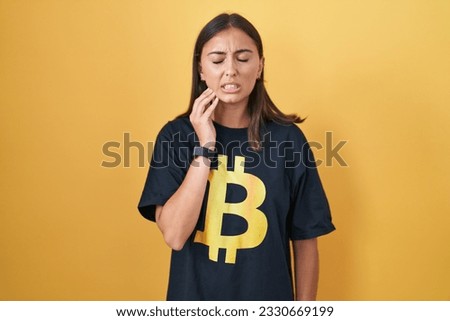 Young hispanic woman wearing bitcoin t shirt touching mouth with hand with painful expression because of toothache or dental illness on teeth. dentist concept. 