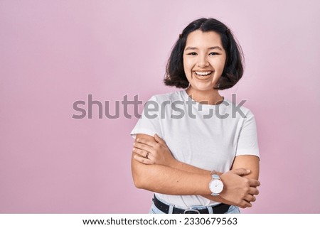 Young hispanic woman wearing casual white t shirt over pink background happy face smiling with crossed arms looking at the camera. positive person. 