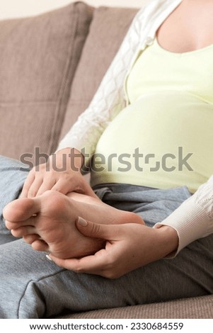 Leg cramps during pregnancy. Closeup of hands massaging swollen foot while sitting on sofa.