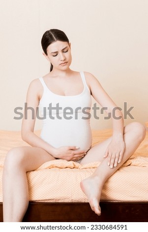 Pretty pregnant woman hands massaging leg sitting on bed.