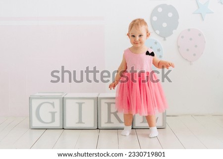Concept of children's emotions. Portrait of lovely toddler little baby child girl with pink dress. Wooden cubes with the inscription girl.