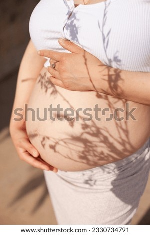 Pregnant belly closeup with floral shadows in boho style. Summer pregnancy.