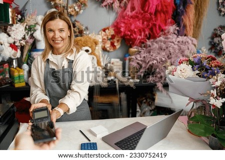 Smiling florist holding POS terminal in floral shop and looking at camera. High quality photo