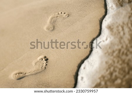 Footprints in sand next to wave. Royalty-Free Stock Photo #2330759957