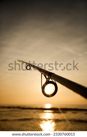 Fishing pole against ocean at sunset.