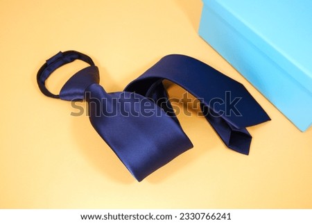 solid blue necktie folded isolated over yellow background with blue gift box close up shot nobody 