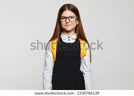 Good looking nerdy pupil kid wearing eyeglasses, school uniform and yellow backpack staring at camera against white background. Back to school concept