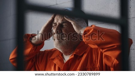 Senior criminal in orange uniform sits on prison bed and dreams about freedom. Prisoner serves imprisonment term in jail cell. Depressed inmate in detention center or correctional facility. Royalty-Free Stock Photo #2330789899