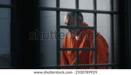 Elderly criminal in orange uniform sits on prison bed and thinks about freedom. Prisoner serves imprisonment term in jail cell. Guilty inmate in detention center or correctional facility. Royalty-Free Stock Photo #2330789929