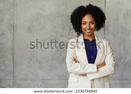Corporate businesswoman cheerful attractive millennial african american lady with bushy hair wearing formal suit posing with arms crossed on chest over gray marble wall at office building, copy space