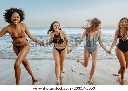Overjoyed young female friends in swimwear having fun and running on the beach, laughing and enjoying their summer vacation on coastline. Summer and holiday concept
