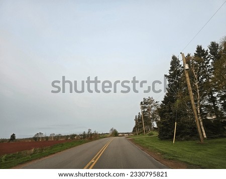 A wide open empty road on an early spring morning through a rural area of Prince Edward Island as the sun rises.
