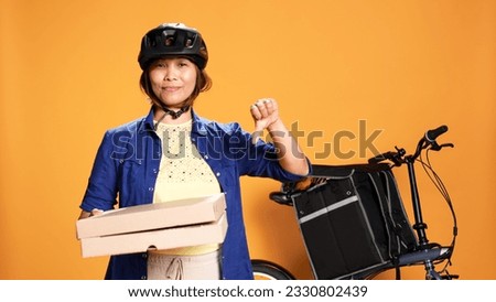 Portrait of professional courier holding fast food pizza boxes, doing dissaproving action. Bike rider showing thumbs down sign while delivering takeaway meal, isolated over studio background