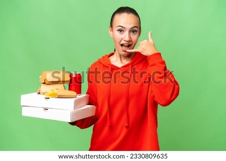 Young Arab woman holding fast food over isolated background making phone gesture. Call me back sign
