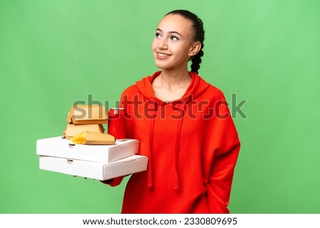 Young Arab woman holding fast food over isolated background thinking an idea while looking up