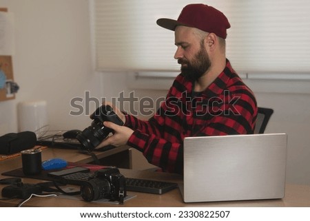 
Photographer at his desk holding a camera. Computers and cameras appear on the scene