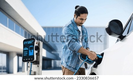 Asian man insert EV charger and recharge his electric car recharging energy from future home charging station. Smart and futuristic home energy infrastructure. Peruse