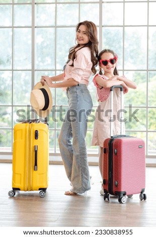 Portrait shot of Asian happy family mom and daughter wearing sunglasses and hat standing with red and yellow trolley luggages look at camera waiting for departure time in airport hallway for vacation. Royalty-Free Stock Photo #2330838955