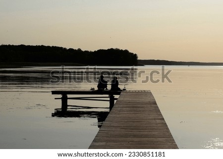 The picture shows two people sitting on the bank of the lake and seeming to enjoy the calmness and natural beauty that surrounds them.

The image looks calm and relaxed, and reflects an atmosphere of 