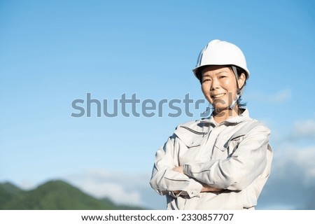 A Japanese woman in work clothes stares into the distance with a serious gaze against the blue sky. Upper body close-up photo with copy space.