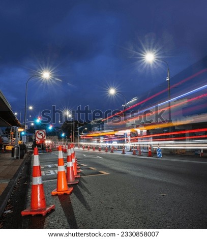 Orange traffic cones lining up the road. Bus light trails approaching the intersection. Roadworks in Auckland. Vertical format.  Royalty-Free Stock Photo #2330858007