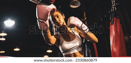 Asian female Muay Thai boxer punching in fierce boxing training session, delivering strike to her sparring trainer wearing punching mitts, showcasing Muay Thai boxing technique and skill. Spur Royalty-Free Stock Photo #2330860879