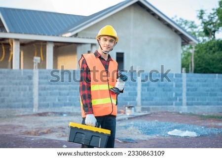 Technician wearing yellow hard hat hand holding a drill and a toolbox