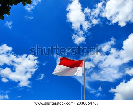 The Indonesian flag flutters above the pole against a blue sky background