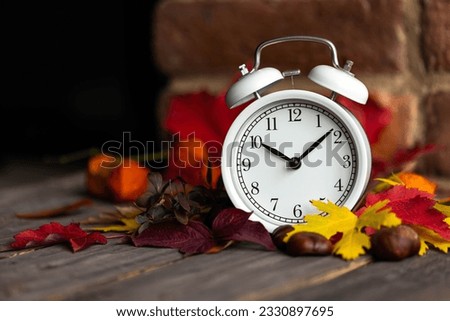 Fall winter time change concept. Autumn composition with retro alarm clock, bright yellow and red leaves, walnut. Brick wall on background. Cozy home atmosphere. Close-up Royalty-Free Stock Photo #2330897695