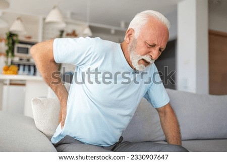 Senior man, with back pain, touches his back, illustrating sciatica and sedentary lifestyle. Emphasizing spine health and the significance of healthcare and insurance in this stock image. Royalty-Free Stock Photo #2330907647
