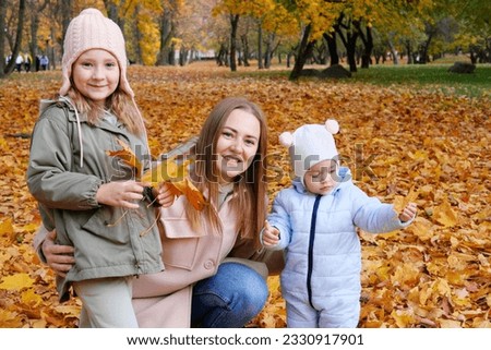 Mother with her daughters collects leaves in the autumn park. Family looking at the camera and smiling. Horizontal photo