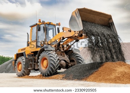 Powerful wheel loader or bulldozer isolated on sky background. Loader pours crushed stone or gravel from the bucket. Powerful modern equipment for earthworks and bulk handling Royalty-Free Stock Photo #2330920505