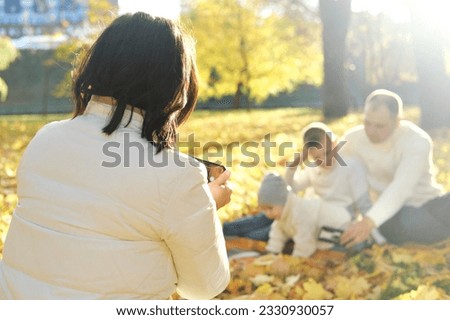A happy family of four spend time in the autumn park. Mother taking pictures of her family or recording video on mobile phone. Horizontal photo