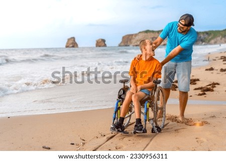 A disabled person in a wheelchair on the beach pushed by a friends by the sea Royalty-Free Stock Photo #2330956311