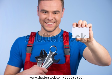 Mechanic holding selection of spanners and business card. smiling man in red overall standing on blue background