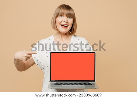 Blonde fun cheerful elderly IT woman 50s years old she wear casual clothes hold use work point on laptop pc computer with blank screen workspace area isolated on plain pastel light beige background