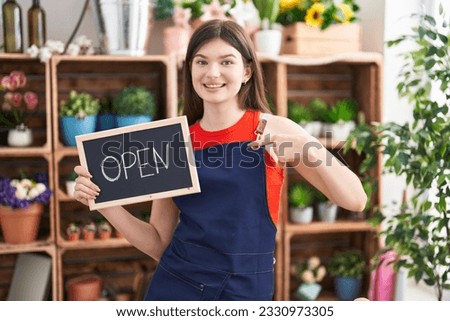 Young caucasian woman working at florist holding open sign pointing finger to one self smiling happy and proud 