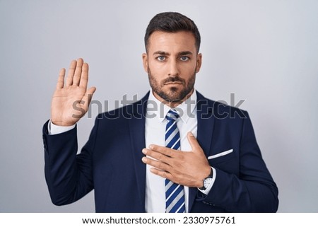 Handsome hispanic man wearing suit and tie swearing with hand on chest and open palm, making a loyalty promise oath  Royalty-Free Stock Photo #2330975761