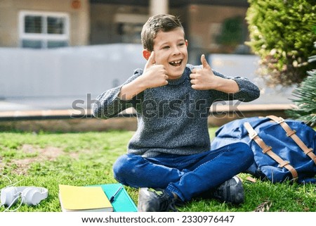 Blond child doing ok gesture sitting on grass at park